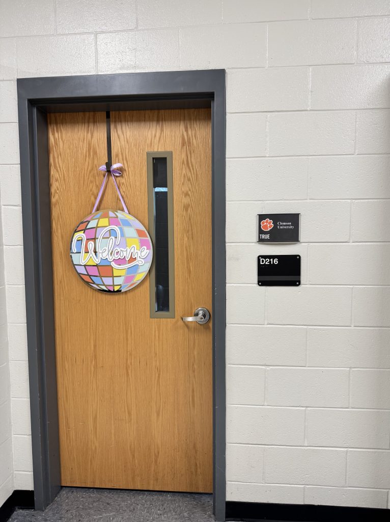Classroom door with colorful disco that says "Welcome" and small sign that says "True" with Clemson University to indicate which classroom door this is for.